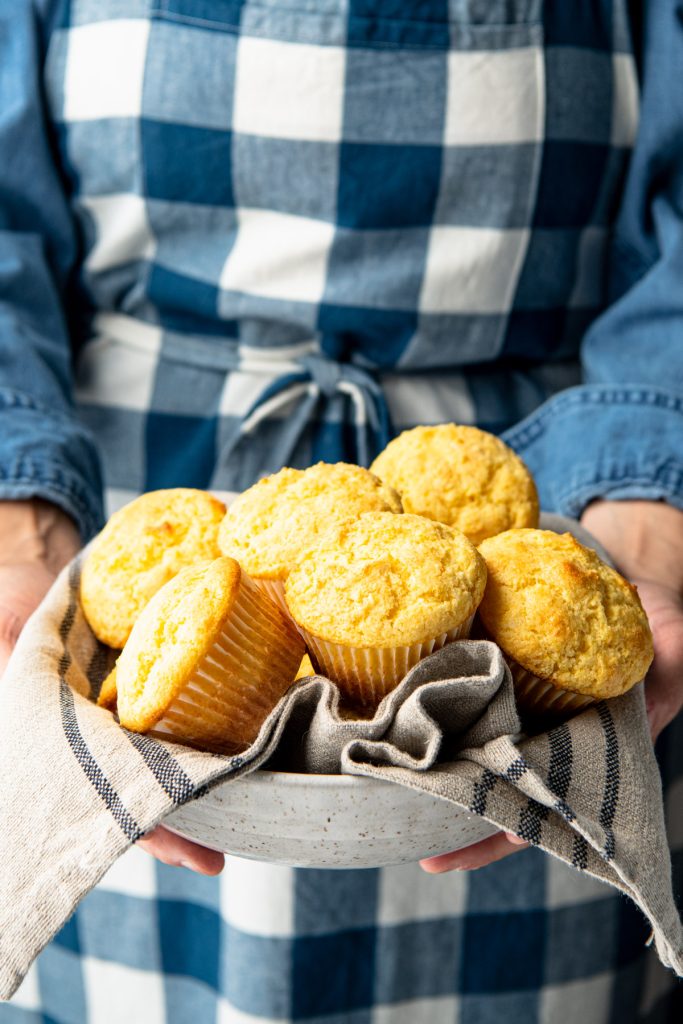 Hands holding a bowl of cornbread muffins