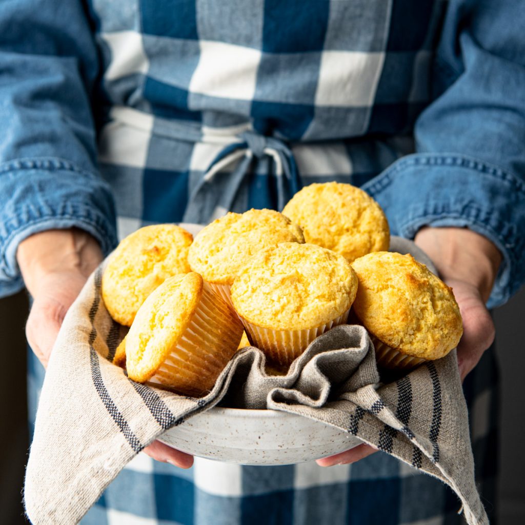 Square image of hands holding a basket of homemade buttermilk sweet cornbread muffins