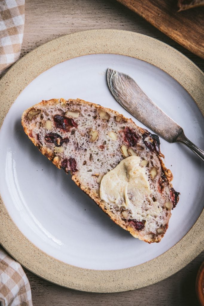 Close overhead image of a slice of no knead cranberry walnut bread on a white plate