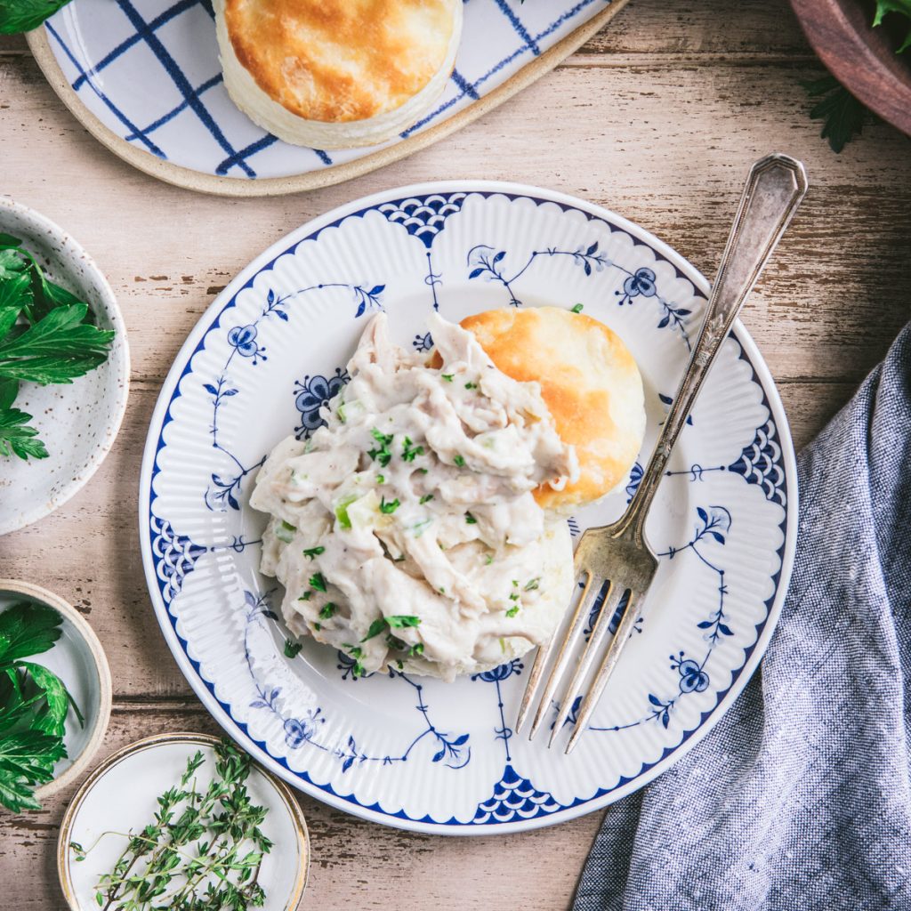 Square overhead shot of a plate of creamed chicken over biscuits on a wooden table