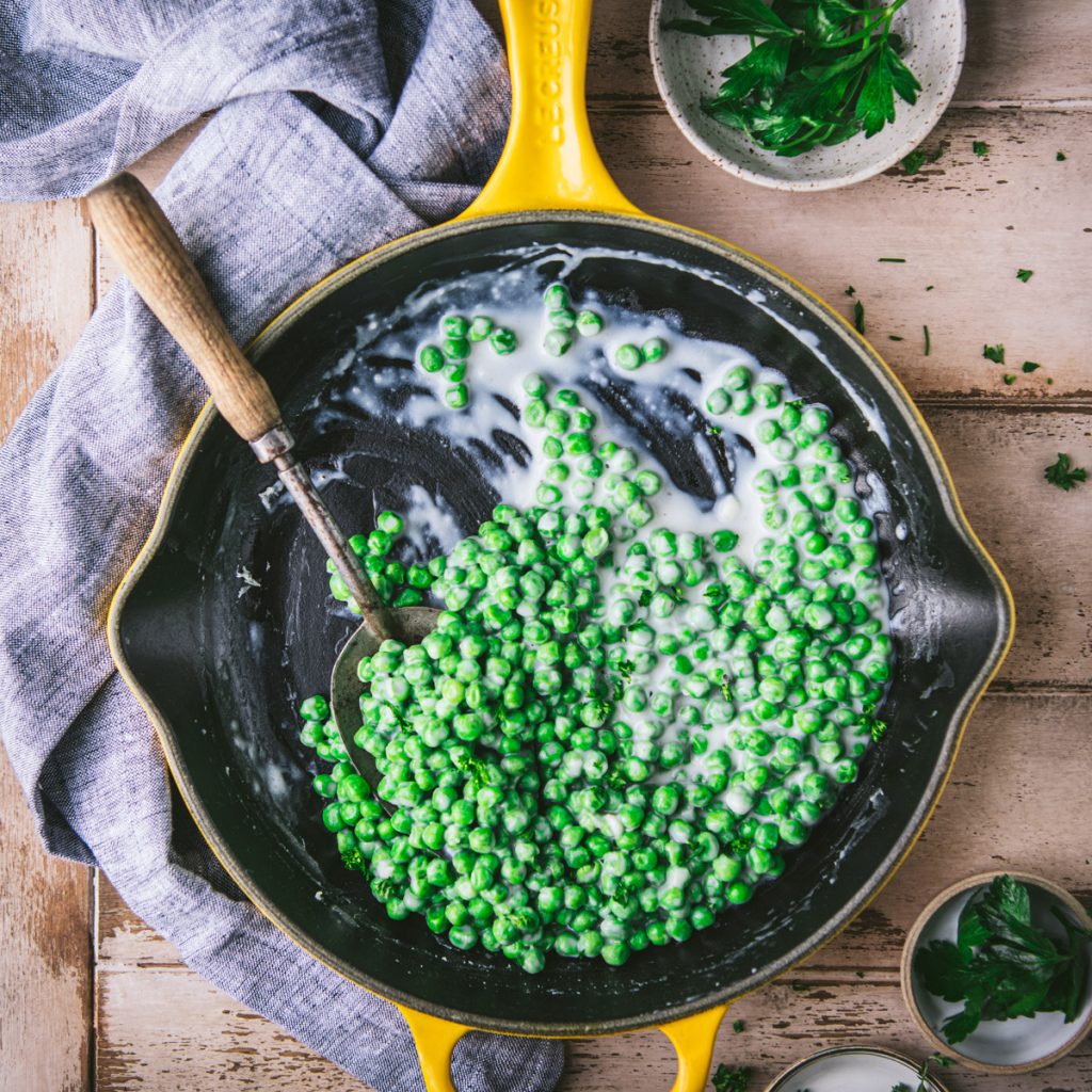 Square overhead image of a cast iron skillet with creamed sweet peas