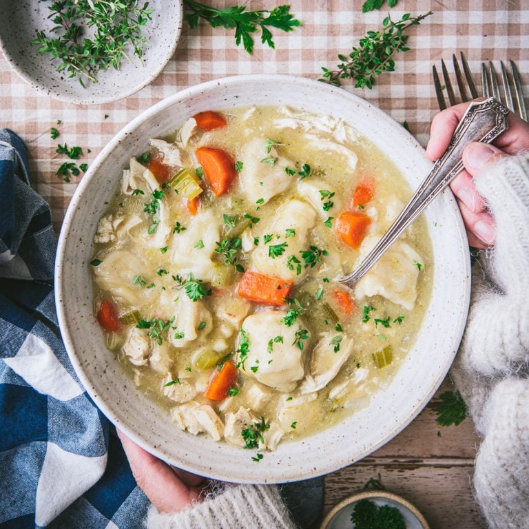 Square overhead image of hands eating a bowl of slow cooker chicken and dumplings