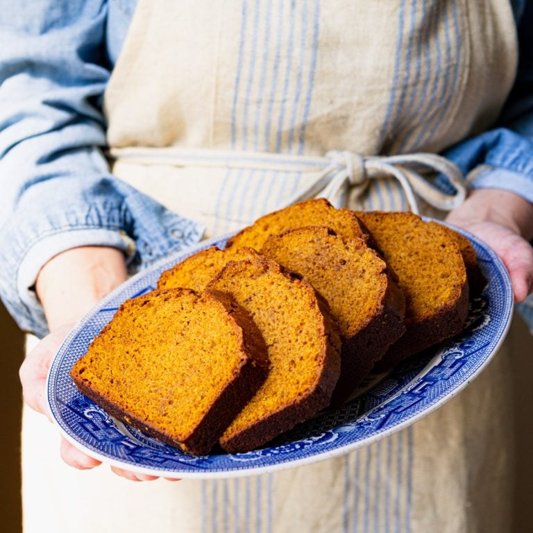 Square image of hands holding a blue and white tray of easy pumpkin bread