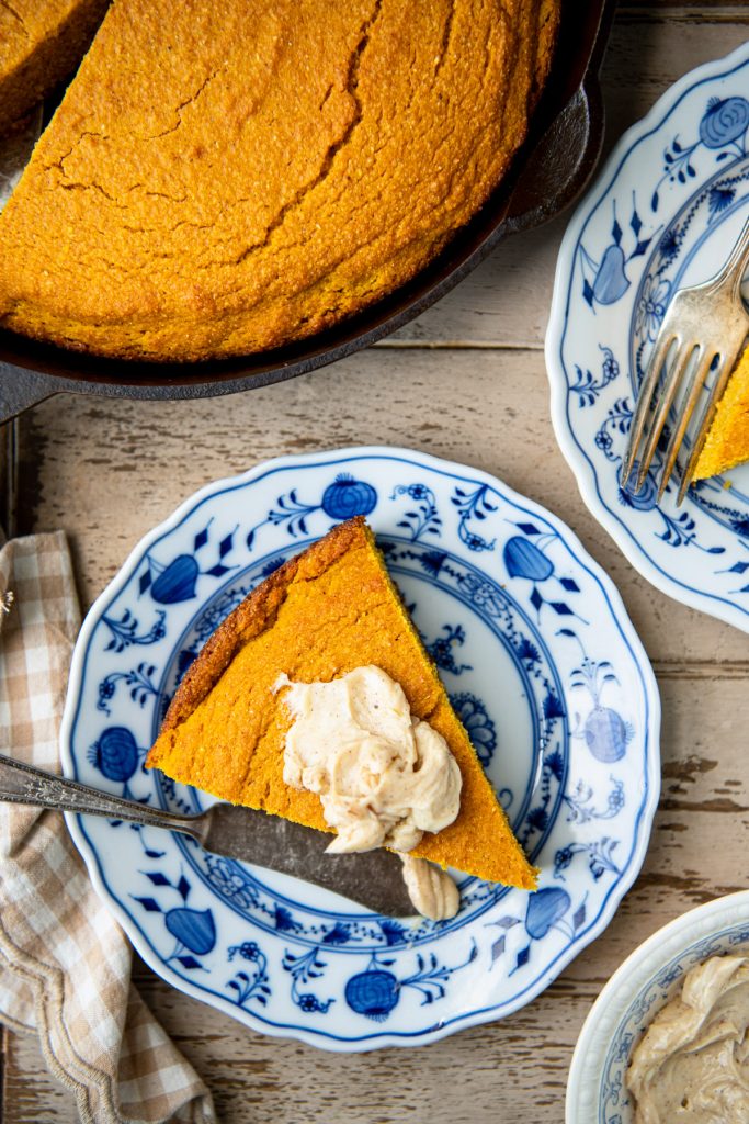 Overhead image of a slice of pumpkin cornbread on a blue and white plate with butter on top