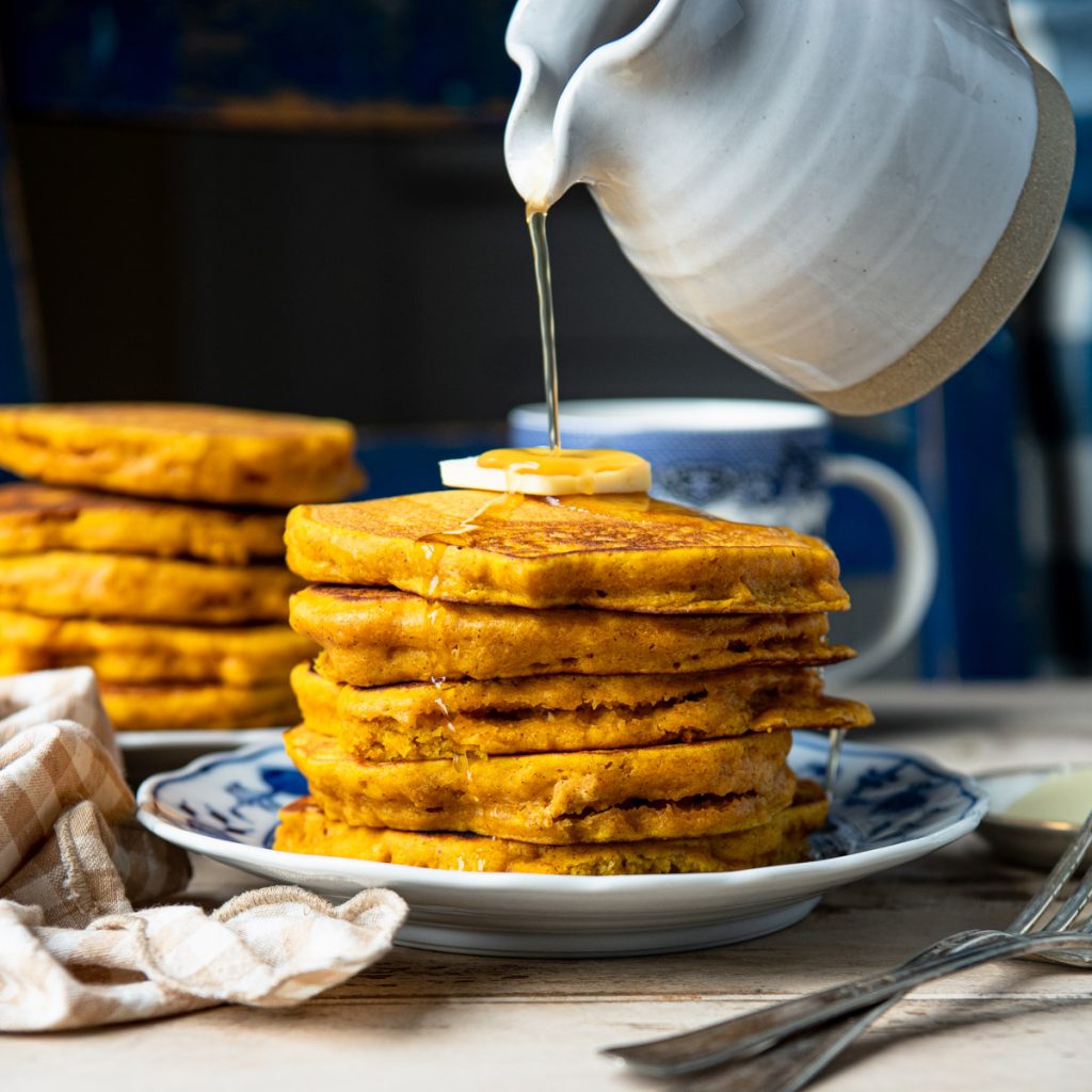 Square image of pouring syrup on a stack of pumpkin pancakes