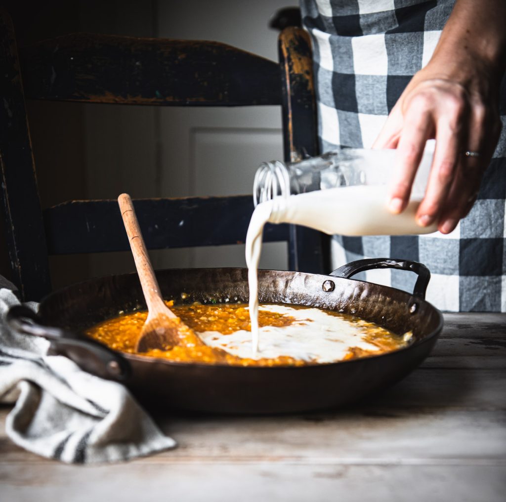 Pouring cream into a skillet of pumpkin pasta sauce