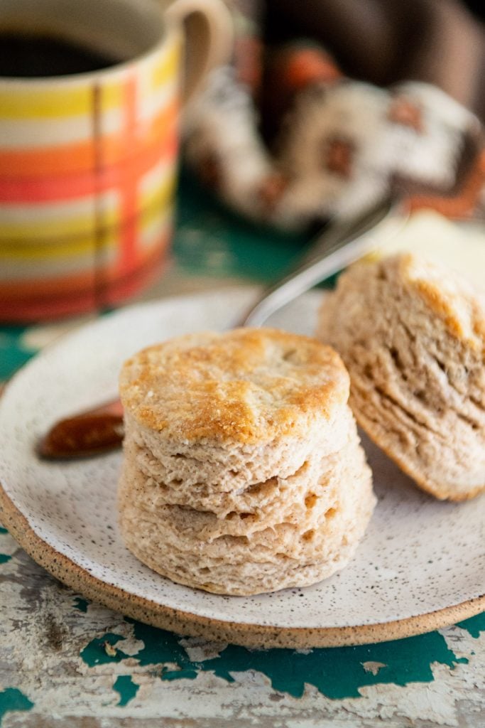Big and fluffy flaky buttermilk biscuit on a plate with coffee in the background