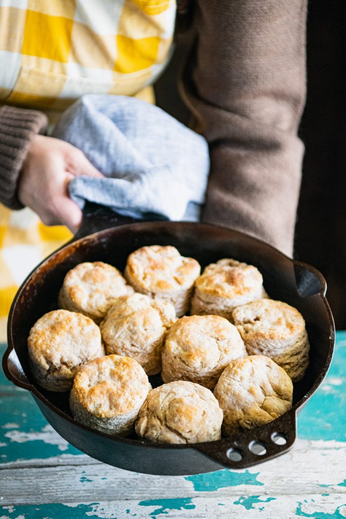 Hands holding a cast iron skillet of biscuits