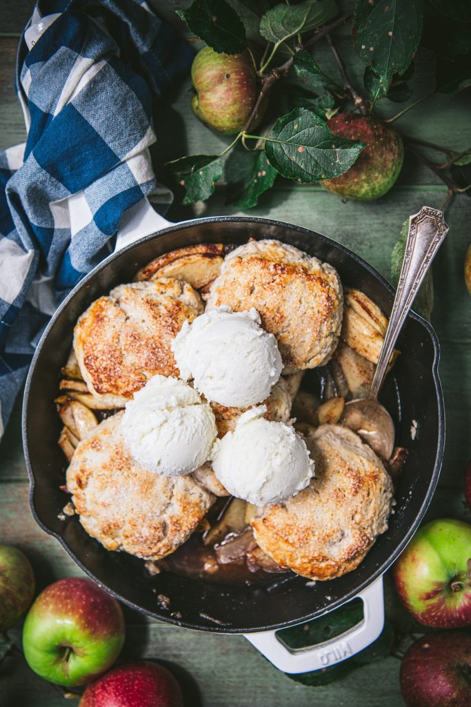 Overhead shot of apple cobbler in a cast iron skillet with ice cream on top