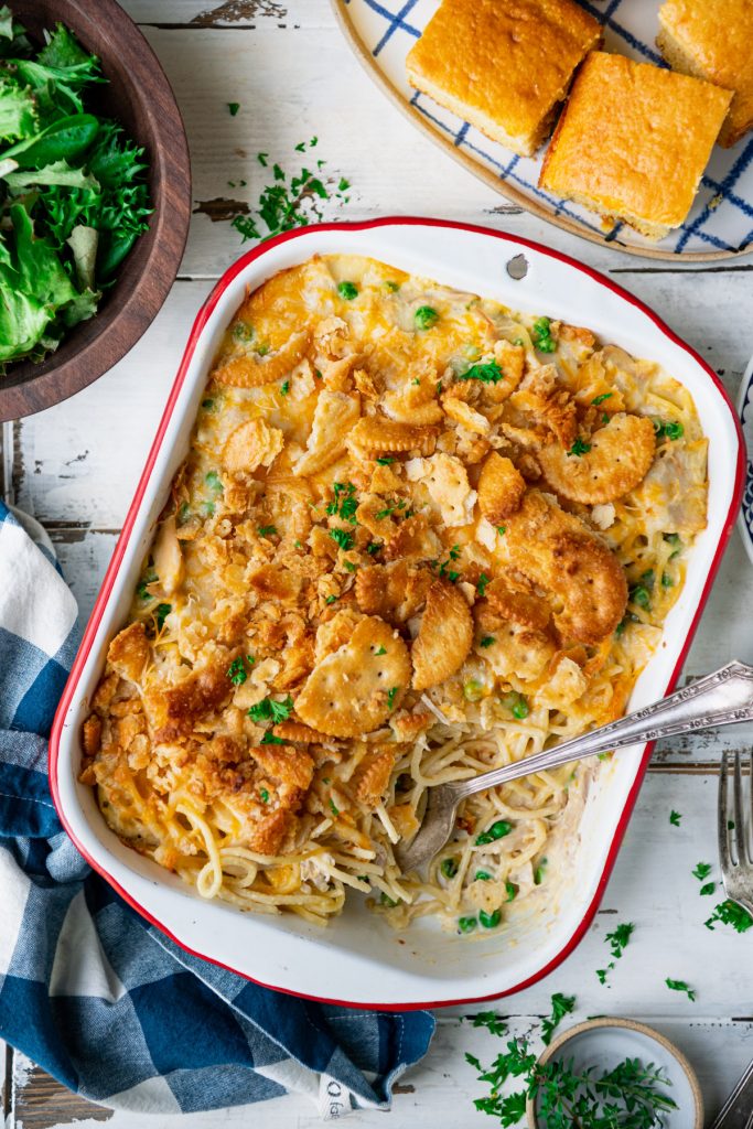 Spoon in a dish of chicken spaghetti casserole with a side salad and cornbread