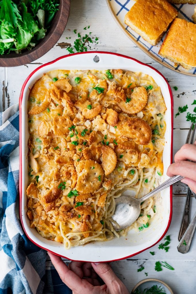 Overhead shot of hands serving a chicken and noodle casserole with a vintage spoon