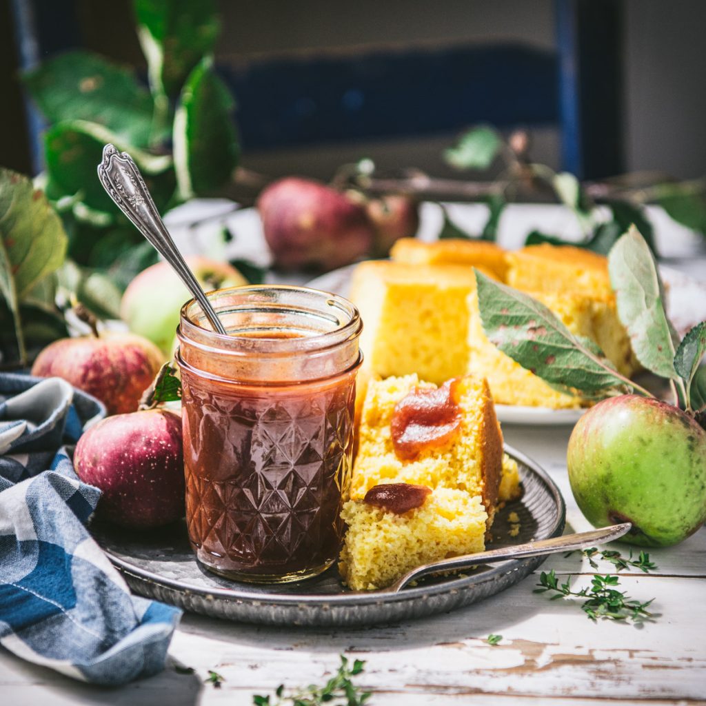 Square side shot of crockpot apple butter in a jar with a plate of cornbread