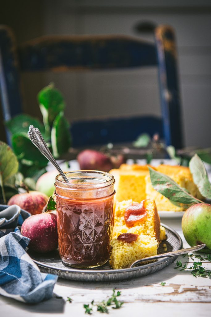 Rustic wooden table with a plate of cornbread and a jar of apple butter