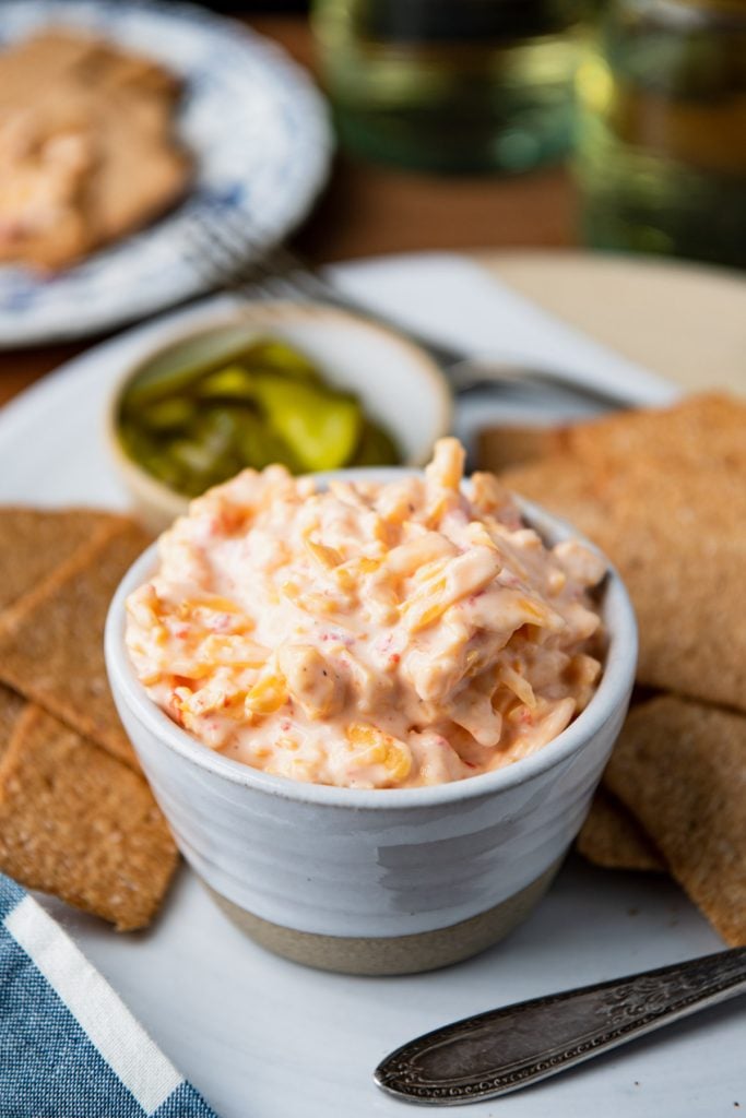Small white bowl full of easy pimento cheese served with crackers and pickles on a white tray