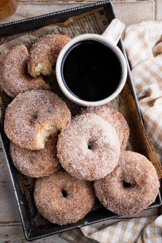Baked apple cider donuts in a metal tray with a mug of coffee