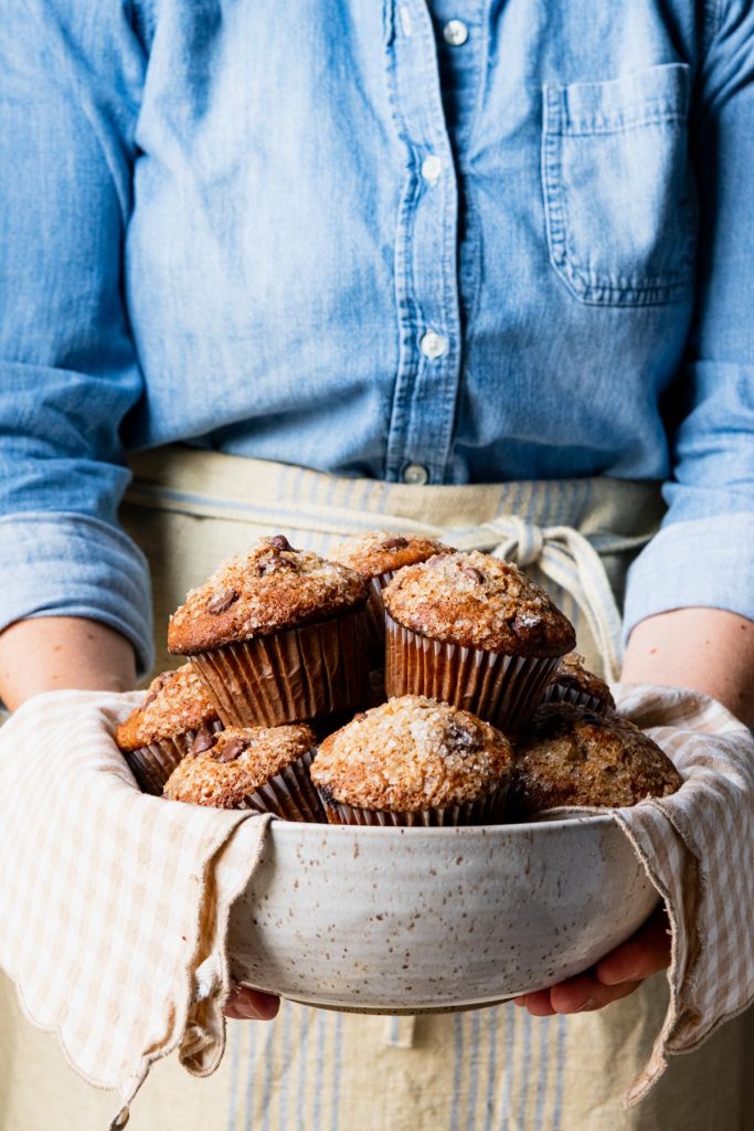 Front shot of hands holding a bowl of banana chocolate chip muffins
