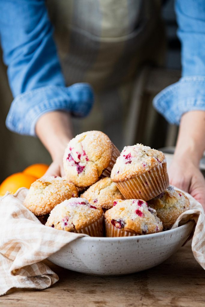 Hands serving a bowl of cranberry orange muffins