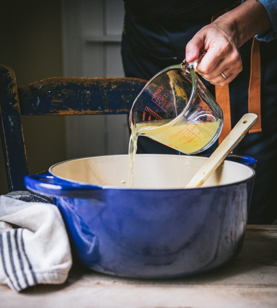 Pouring chicken broth into a Dutch oven