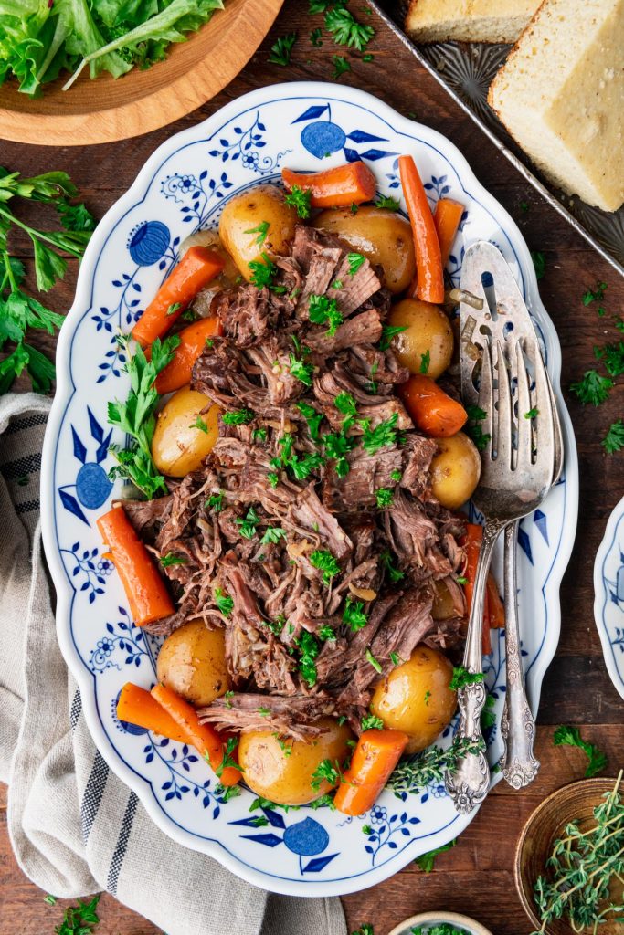 Overhead image of slow cooker pot roast on a table with serving utensils