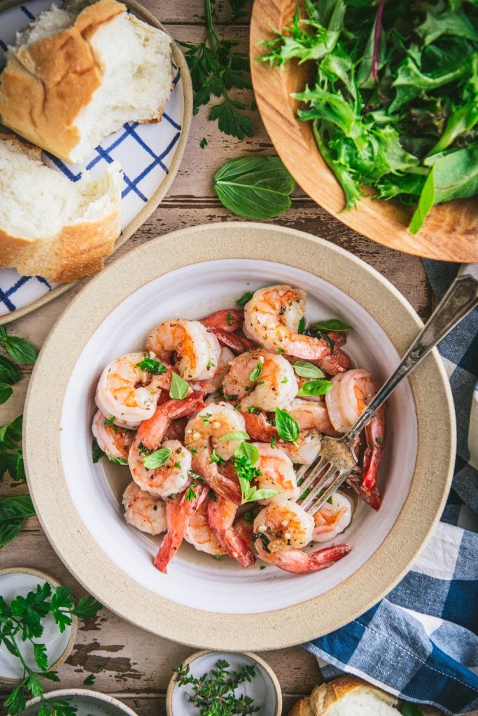 Overhead image of a bowl of garlic shrimp with a side salad and bread