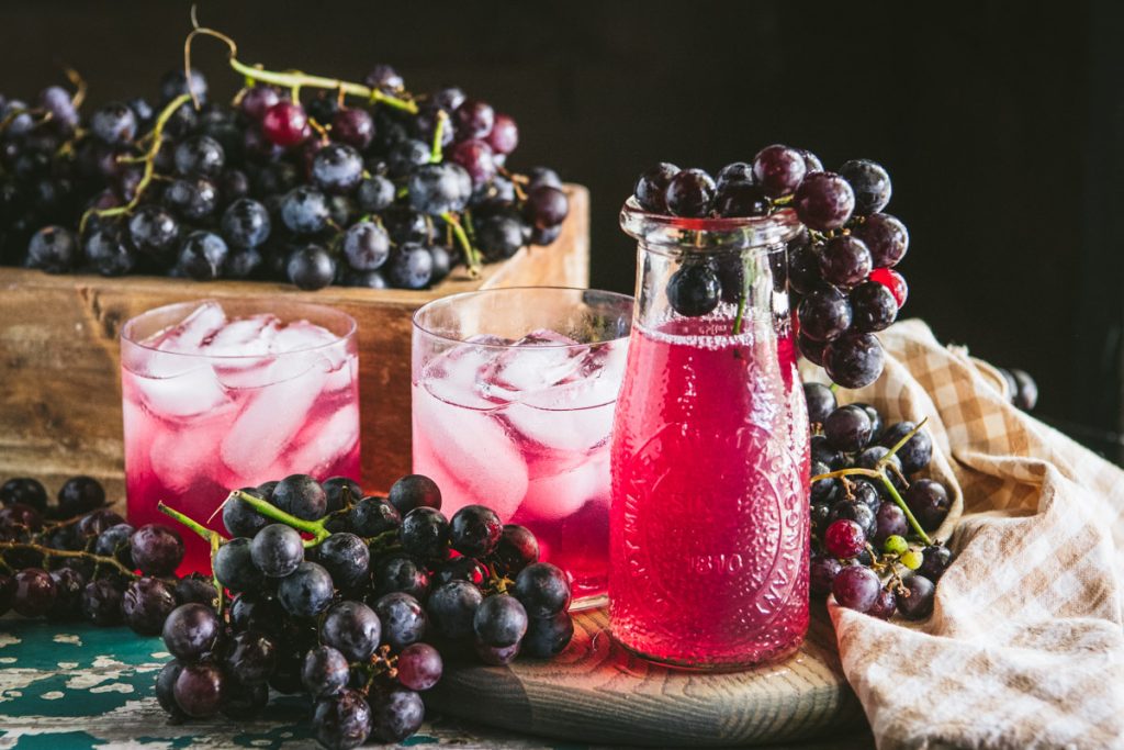 Horizontal image of a jar and glasses of homemade concord grape juice on a table