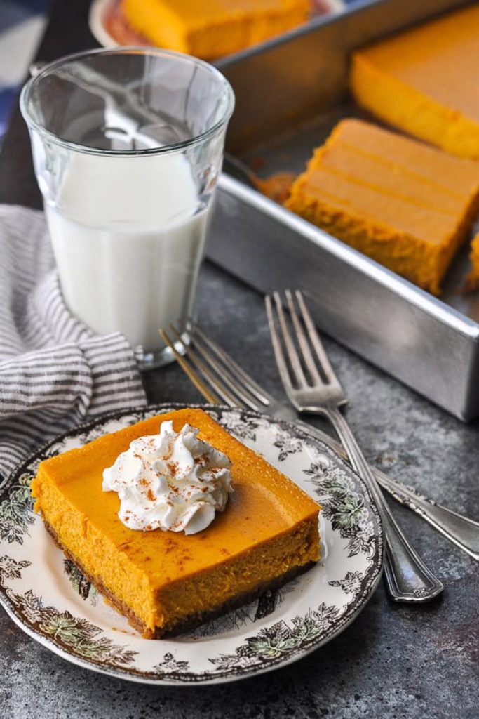 Pumpkin cheesecake bars on a table with a glass of milk