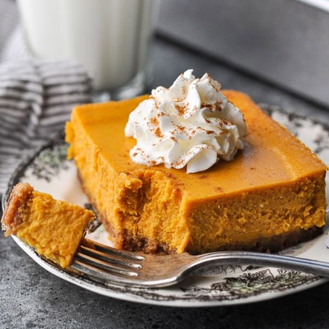 Square side shot of pumpkin cheesecake bars on a plate with whipped cream on top