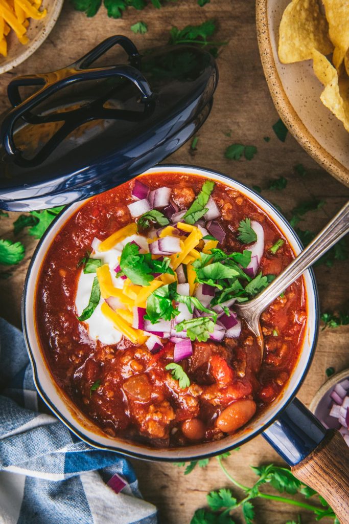 Overhead image of a bowl of taco chili with a side of tortilla chips on a dinner table
