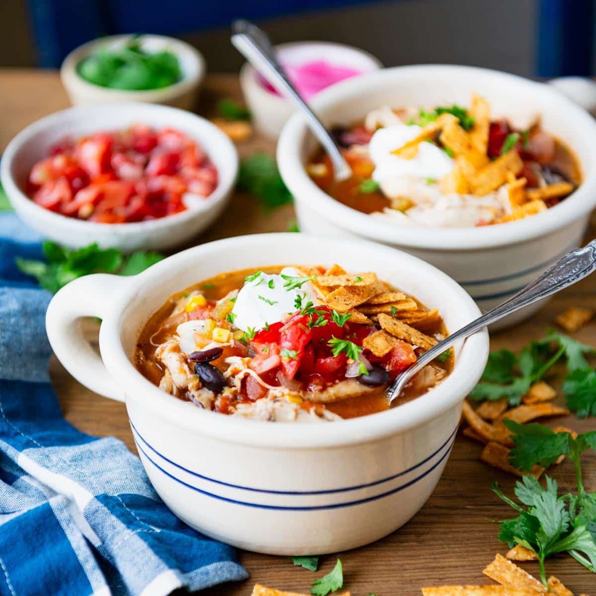 Square side shot of two bowls of slow cooker chicken tortilla soup on a dinner table.