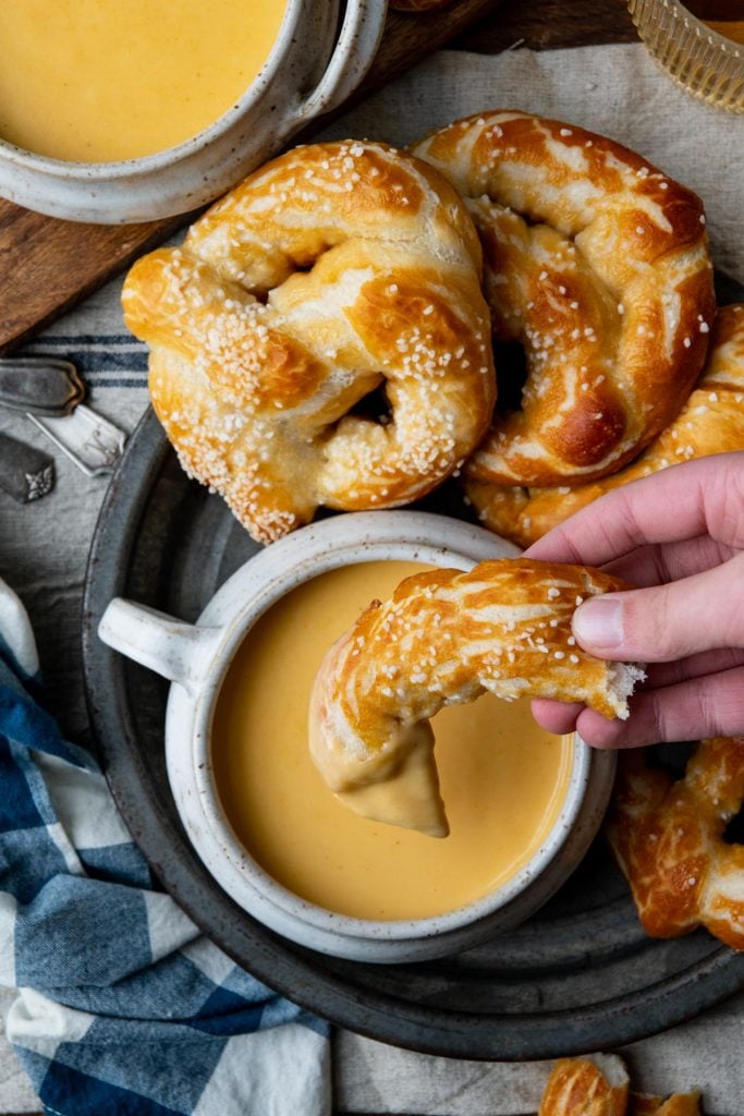 Overhead image of hand dipping a chunk of soft pretzel in homemade beer cheese dip