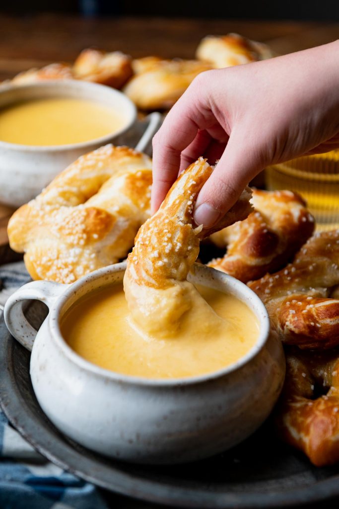 Hand eating beer cheese dip with a pretzel