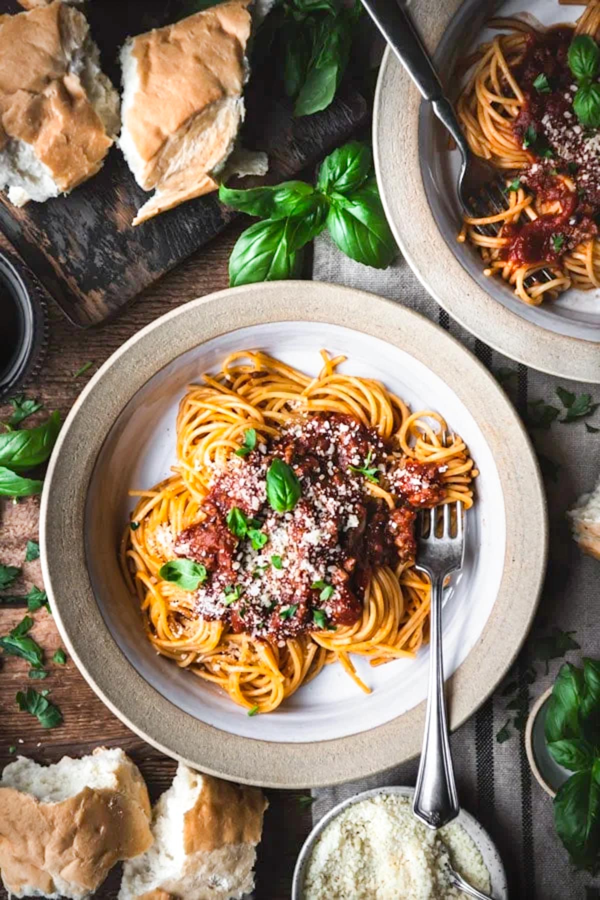An overhead shot of a bowl of spaghetti topped with a homemade stovetop spaghetti sauce, garnished with grated parmesan cheese and fresh basil leaves.