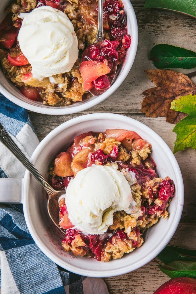 Overhead shot of apple cranberry crisp in white bowls with vanilla ice cream on top