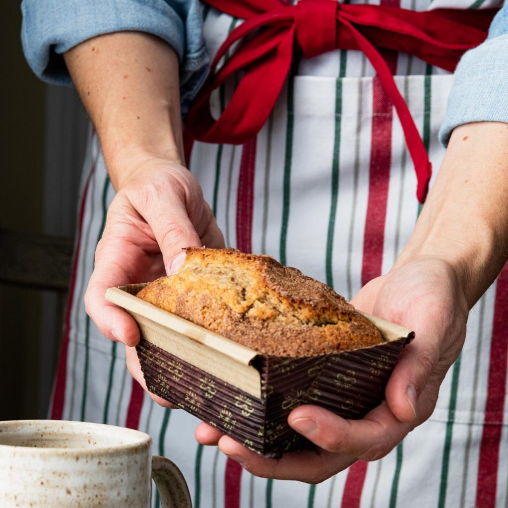Square image of hands holding a loaf of date nut bread