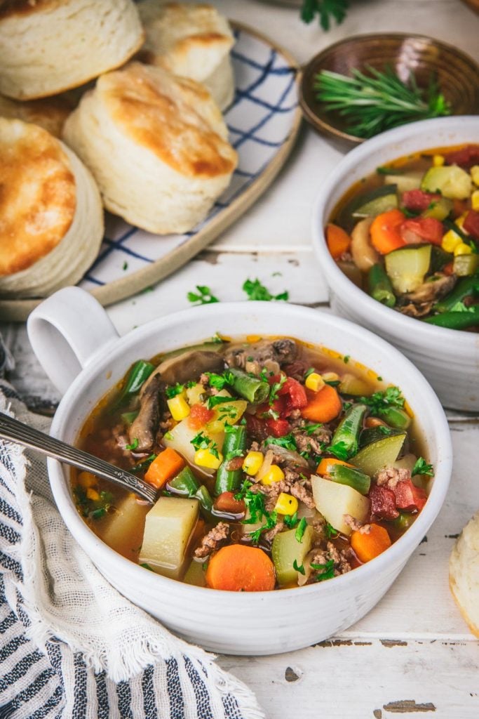 Close up front shot of a bowl of hamburger soup with biscuits and salad in the background