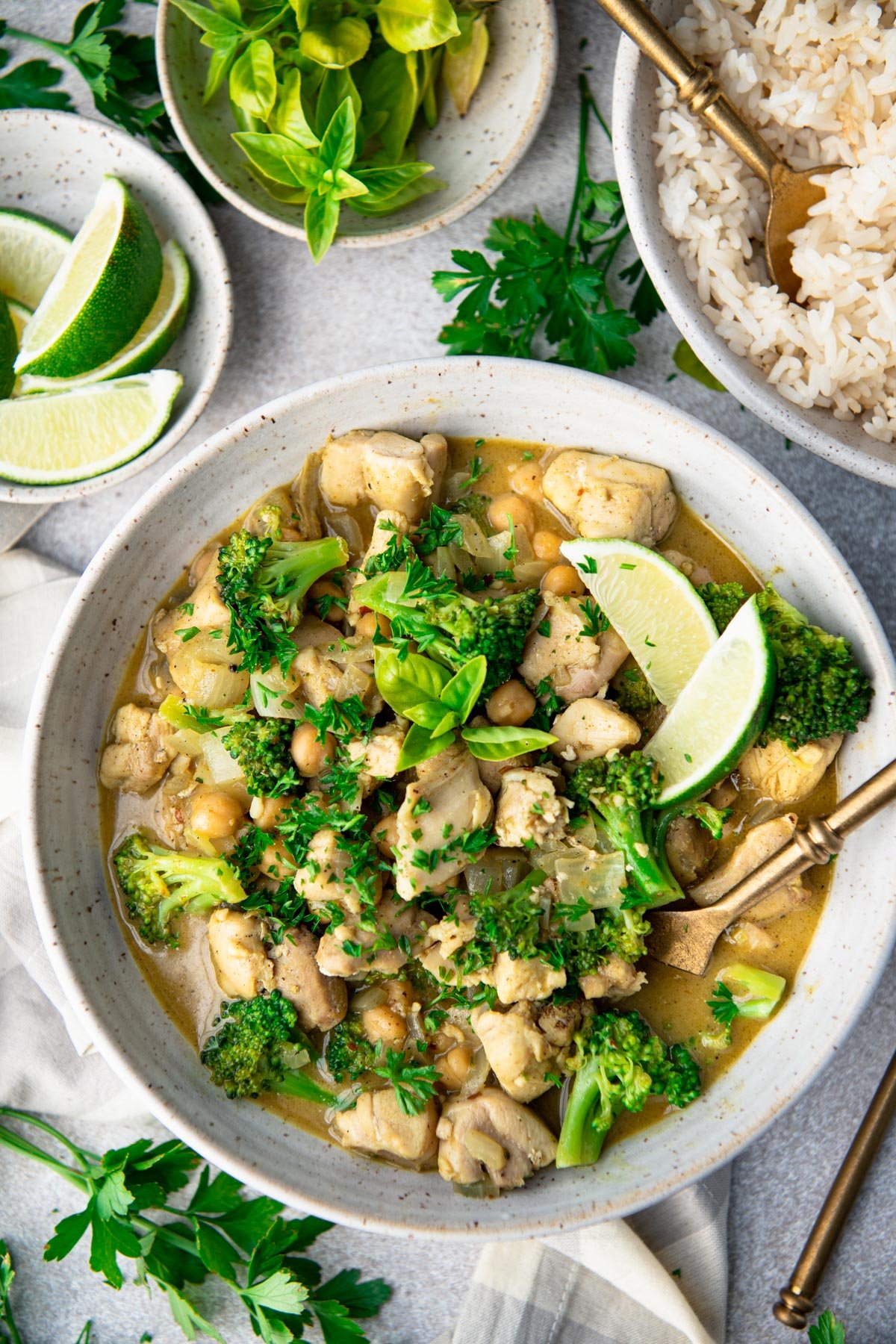 Bowl of chicken coconut curry on a table with lime wedges and parsley