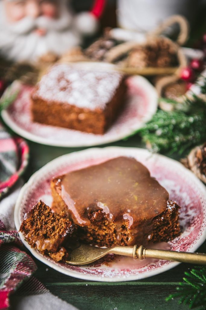 Close up front shot of a slice of old fashioned gingerbread cake on a red and white plate with lemon sauce