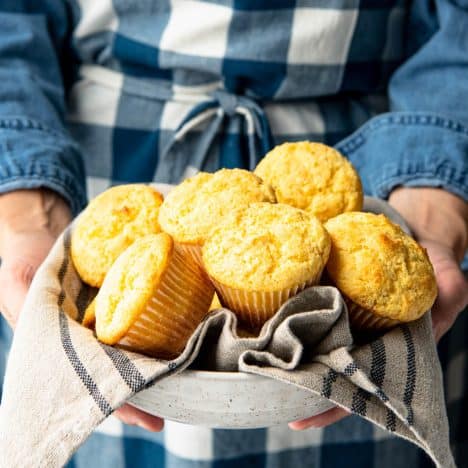 Square side shot of a woman holding a bowl of corn muffins.