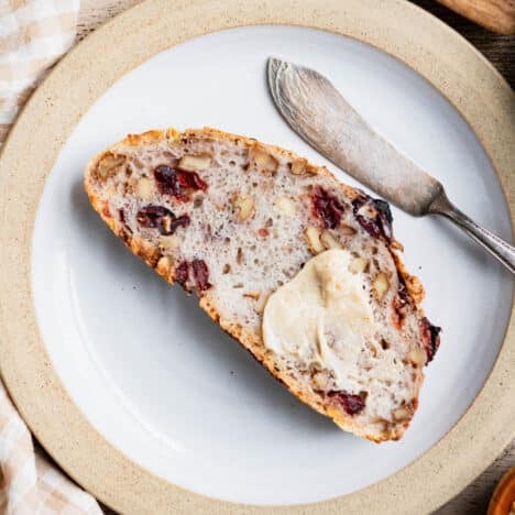 Square overhead image of cranberry walnut bread slice on a plate.