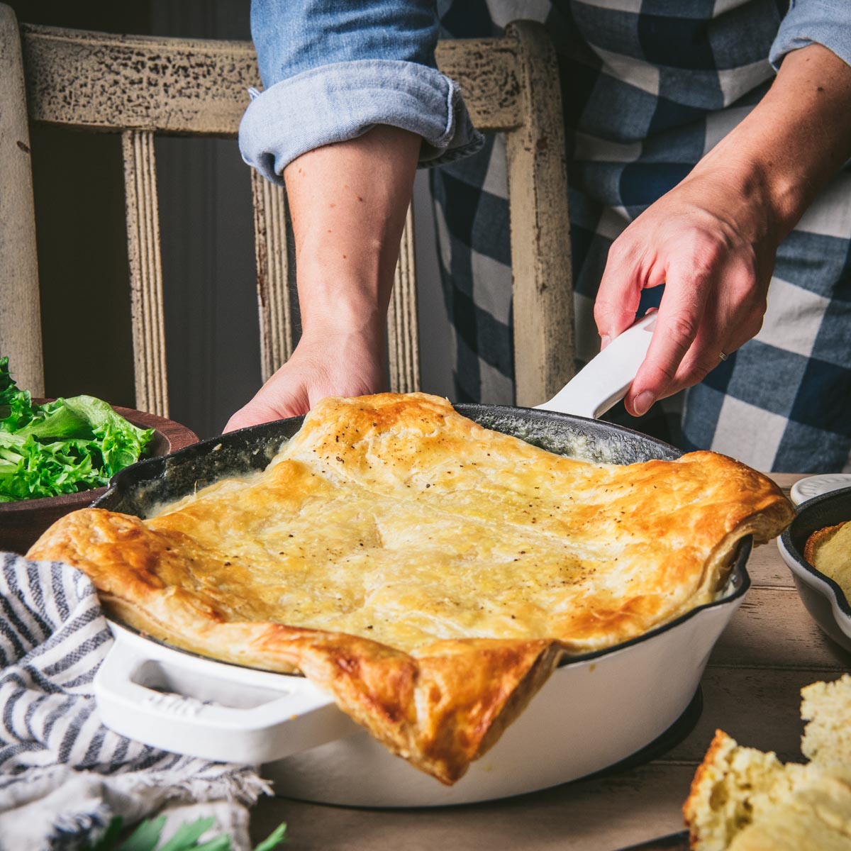 Square side shot of hands holding a skillet of chicken pot pie with puff pastry