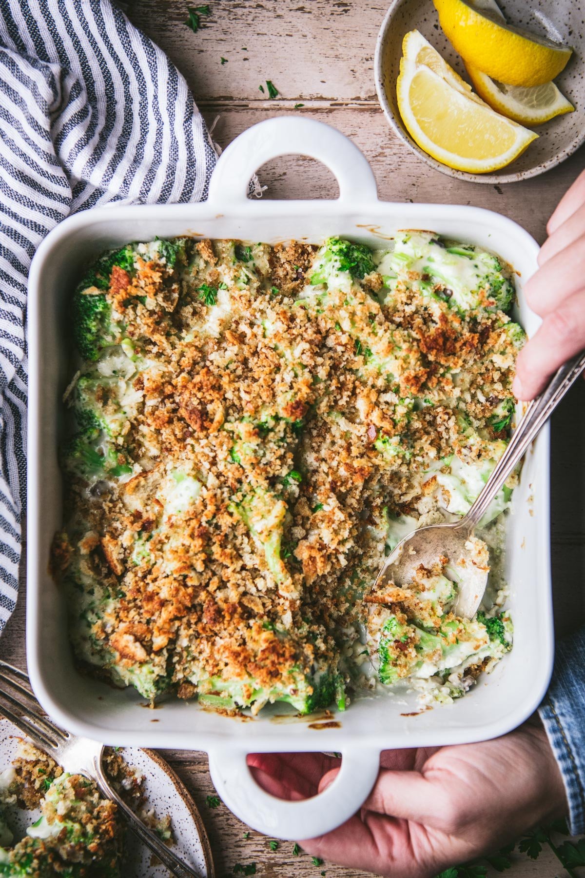 Overhead shot of hands serving an easy broccoli casserole from a white dish