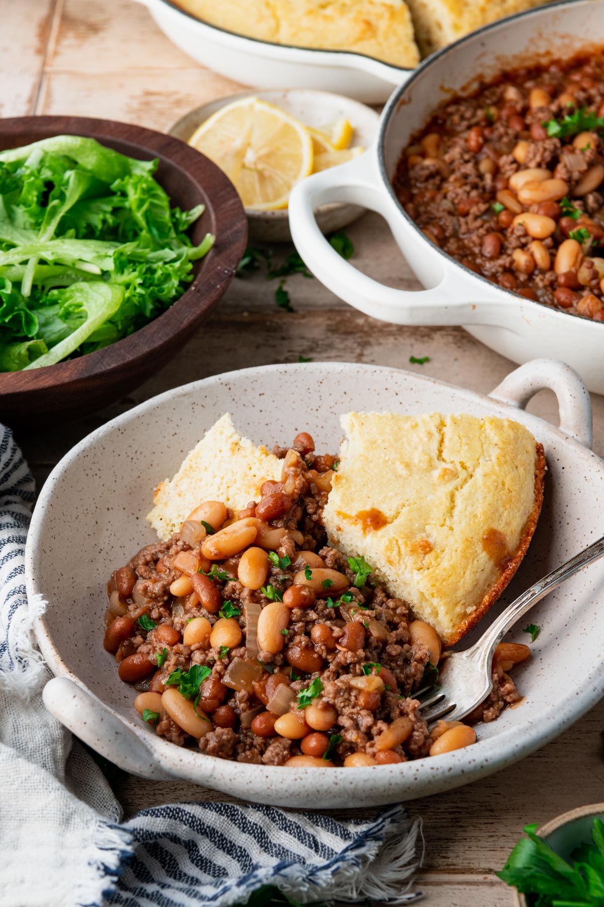Side shot of a dish of baked bean casserole with cornbread on a dinner table