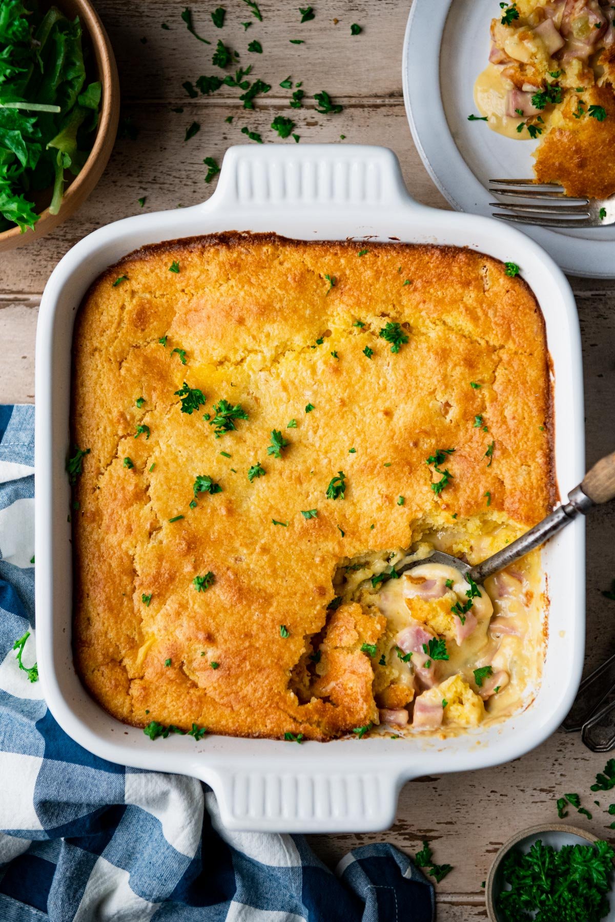 Overhead image of ham casserole with cornbread topping on a table with side salad
