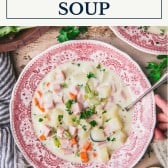 Hands holding a bowl of ham and potato soup with text title box at top