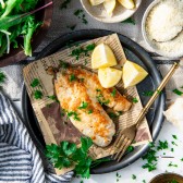 Overhead shot of baked tilapia recipe served with lemon wedges and fresh herbs on a plate