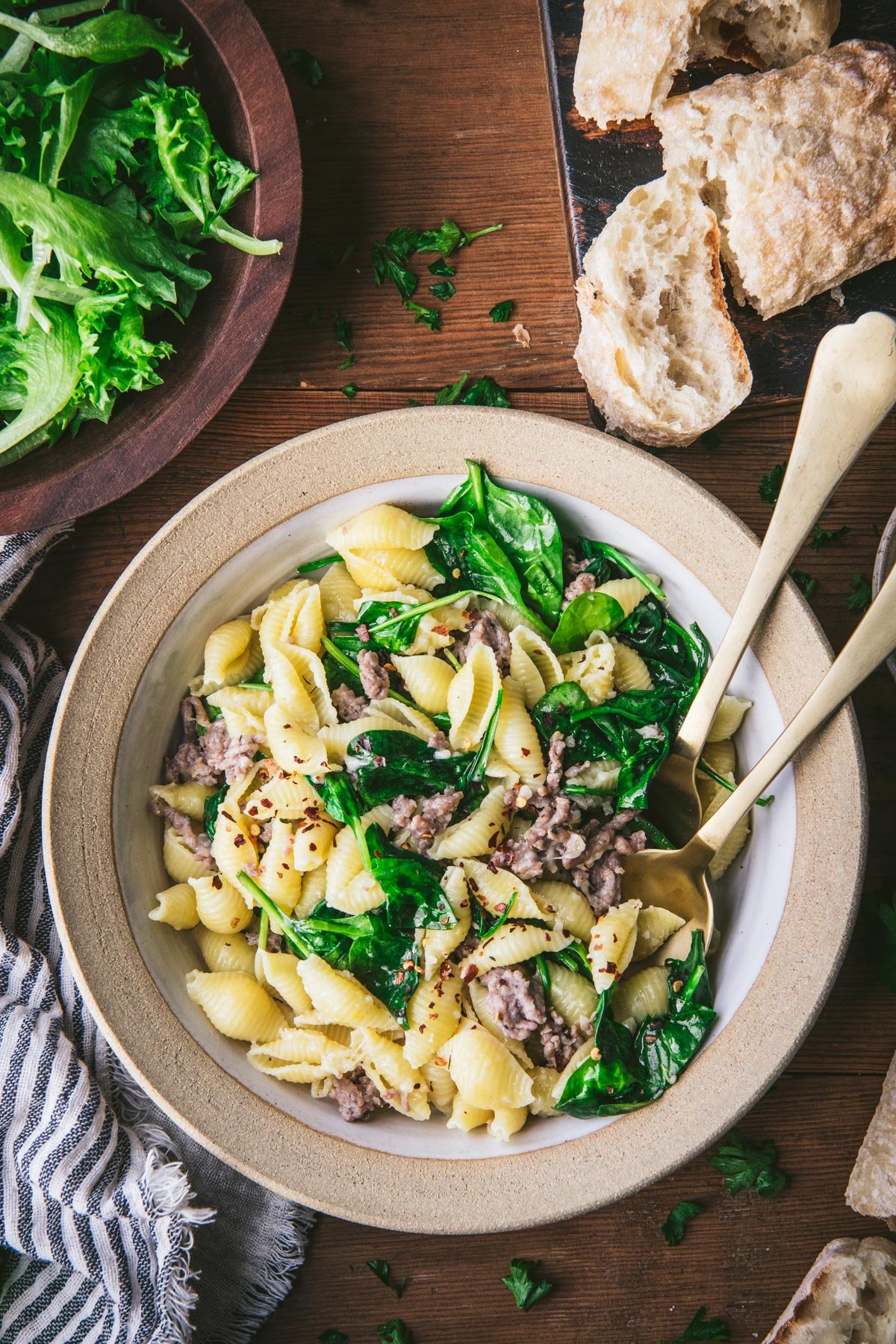 Overhead shot of a bowl of pasta with sausage and spinach on a wooden table