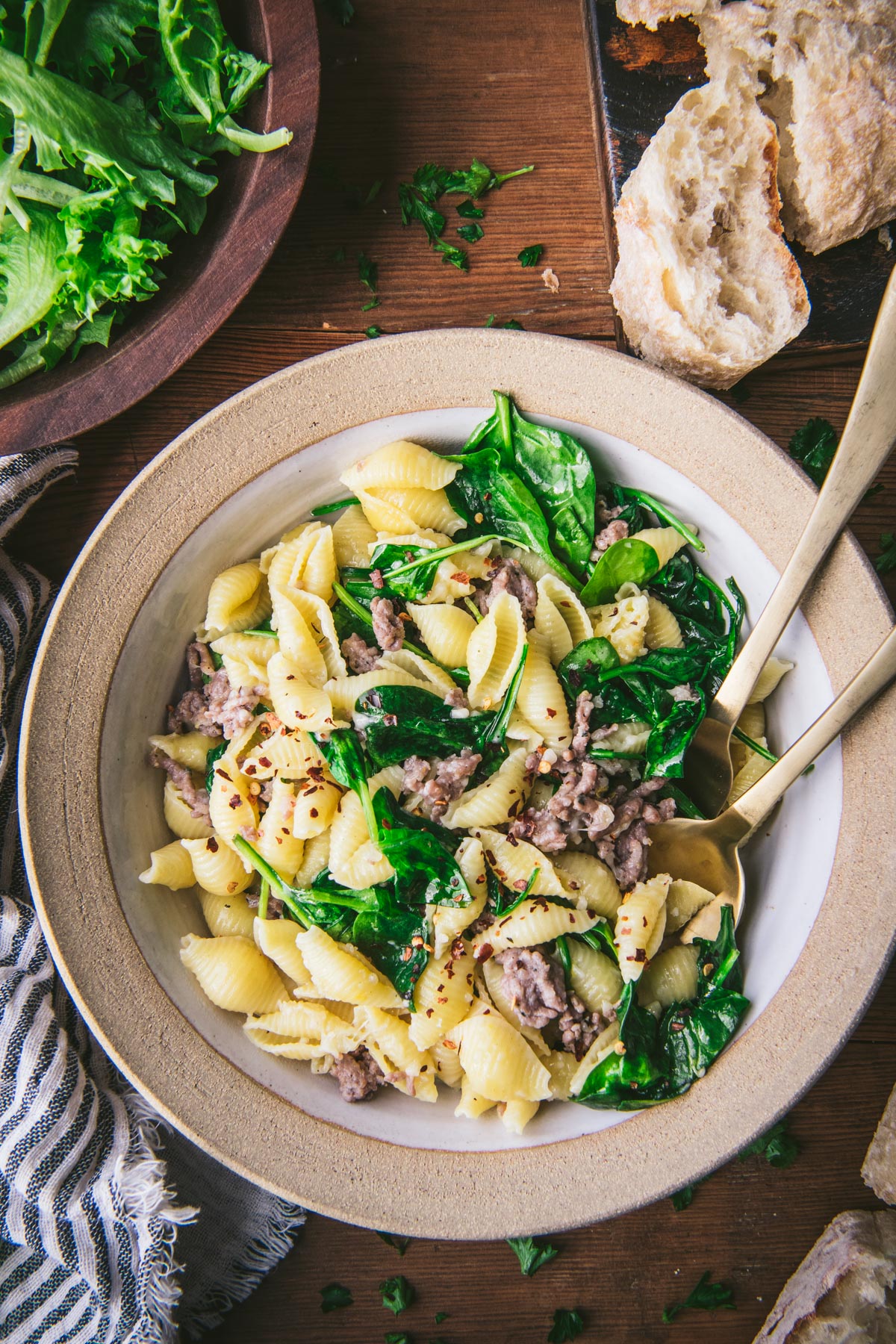 Close overhead image of pasta with Italian sausage and spinach on a table with salad and bread