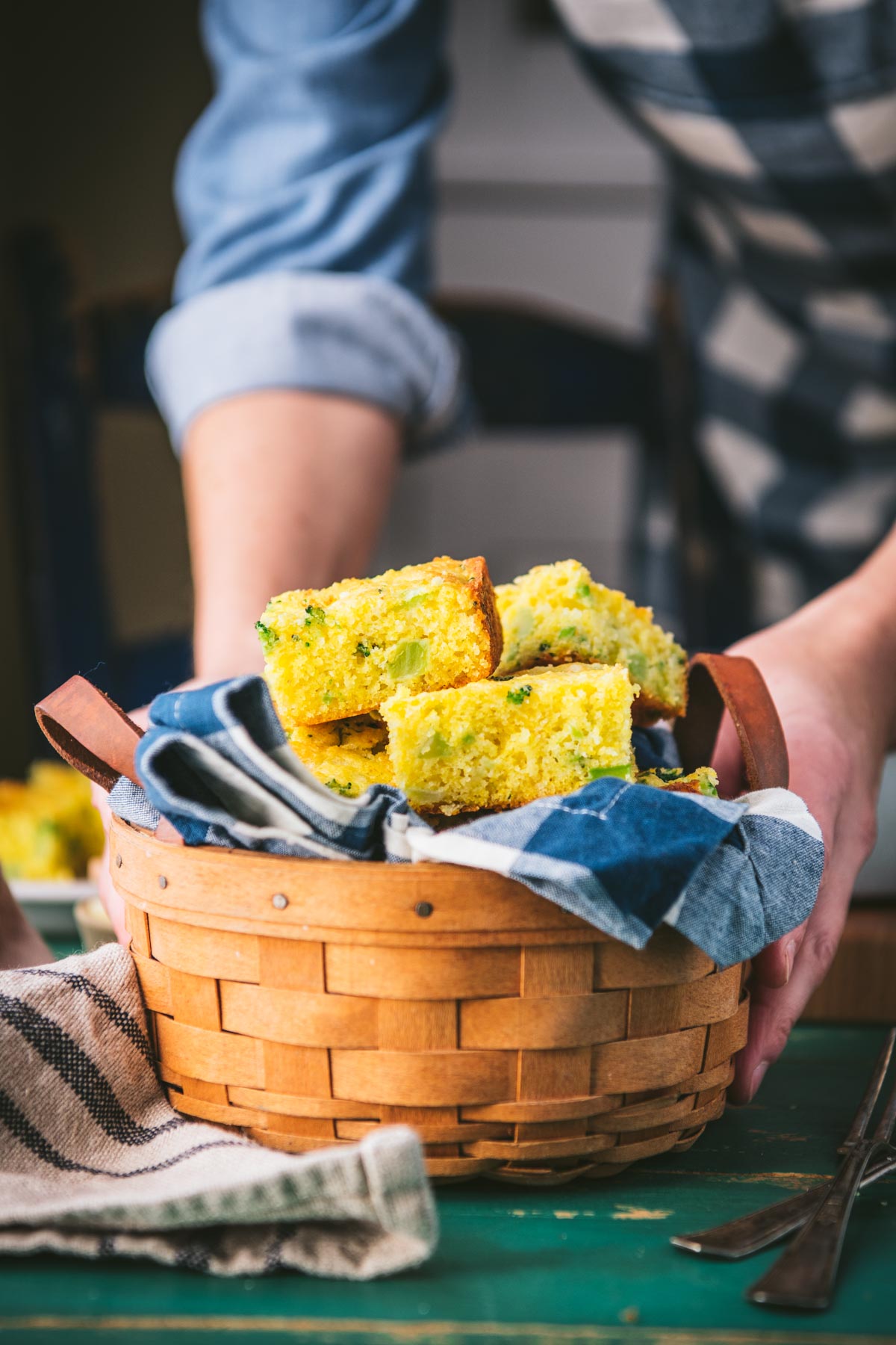 Hands serving a basket of broccoli cornbread on a table