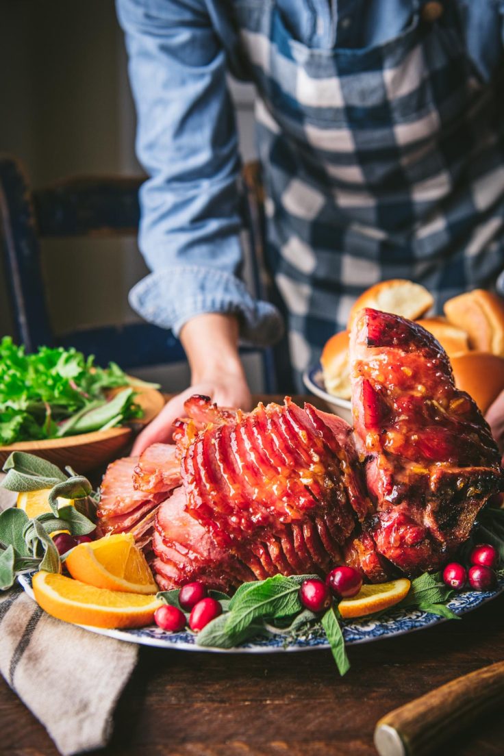 Hands serving a brown sugar bourbon glazed ham on a holiday table