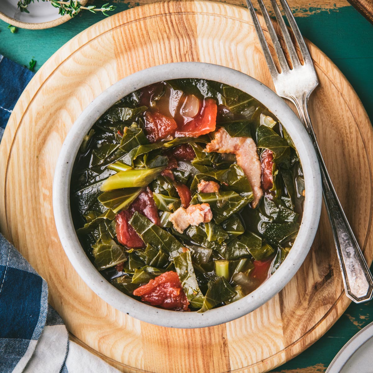 Square overhead image of a bowl of collard greens with bacon and tomatoes on a wooden plate